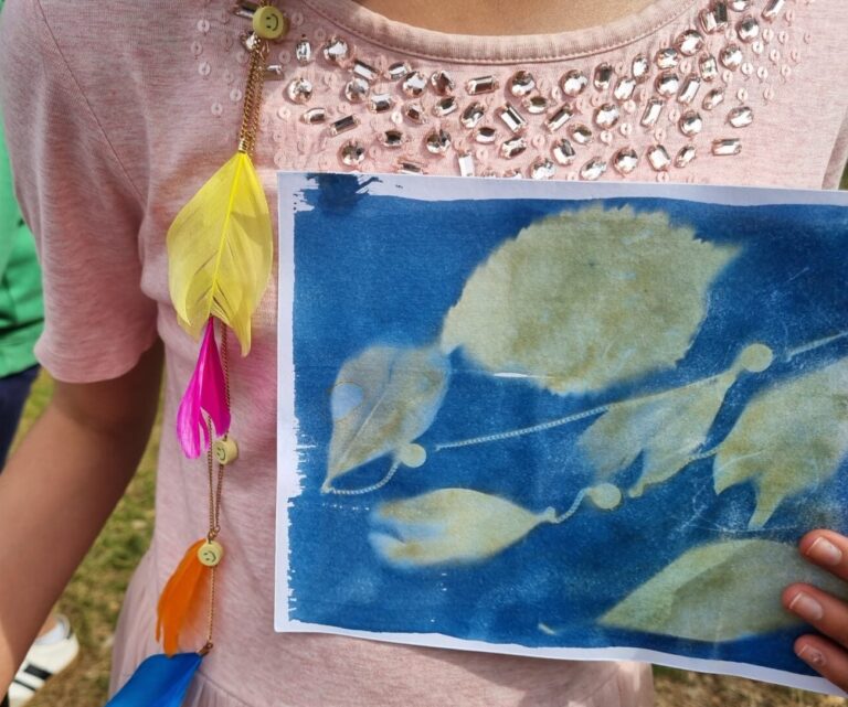 Child, in a pink dress holds a cyanotype print of leaves